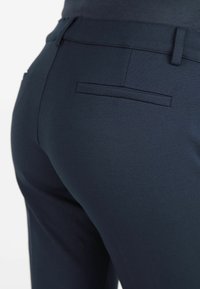 Marineblauwe op maat gemaakte broek met een gladde textuur, voorzien van een achterzak en nette stiksels, die een getailleerd ontwerp benadrukken.