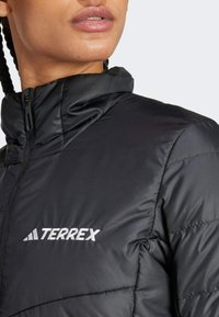 Svart isolerad jacka med hög krage, med quiltad textur och dragkedja fram. Varumärket "TERREX" är broderat i vitt.