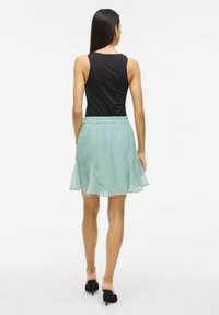 Bezrękawnik w kolorze czarnym połączony z jasnorozowy plisowaną spódnicą z zebranym pasem i przezroczystą teksturą. Czarne klapki na obcasie.