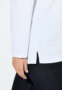 Witte katoenen overhemd met lange mouwen en zijopeningen, gecombineerd met donkerblauwe denim jeans. Zachte textuur en casual ontwerp.