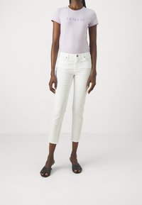 Světle fialová košile s krátkým rukávem s logem "Armani Exchange", zkombinovaná s bílými zkrácenými džíny a černými žabkami. Hladká tkanina a přiléhavý design.