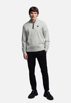 Suéter gris de pullover con cuello de media cremallera y un diseño de puntos negros. Combinado con pantalones negros y zapatos negros gruesos para un look moderno.