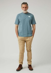 Camiseta de algodón azul claro con mangas cortas, con un pequeño estampado en el pecho. Pantalones beige de corte ajustado y botas marrones con cordones.