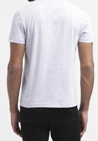 Grå kortärmad t-shirt med rund halsringning, med en mjuk textur och rak skärning, sedd bakifrån. Svarta byxor syns nedanför.