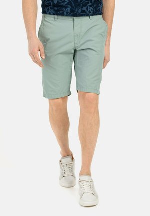 Hellgrüne Shorts mit einer glatten Textur, knielang und im klassisch geschnittenen Stil, kombiniert mit weißen High-Top-Sneakern.