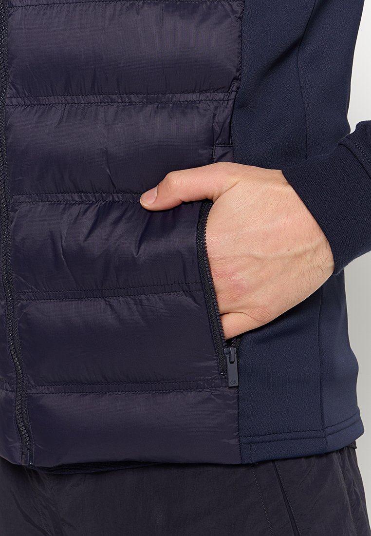 Gilet rembourré bleu marine au toucher lisse, doté d'une poche zippée et de panneaux latéraux contrastants. Conçu pour la chaleur et la fonctionnalité.