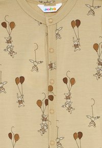 Beige baby overall med knäppning, dekorerad med bruna och bruna kaniner som håller i ballonger i olika lekfulla poser.