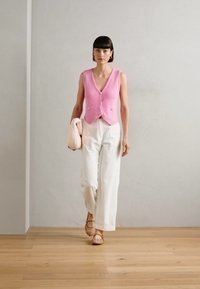 Chaleco de punto rosa con detalles de botones combinado con pantalones de pierna ancha a rayas blancas y sandalias beige. Texturas suaves, diseño minimalista.