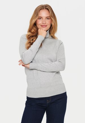 Pull à col roulé gris clair avec des poignets et un ourlet côtelés, associé à un jean bleu foncé. Texture douce, design ajusté, style minimaliste.