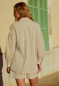 Gestreepte beige shirt met pofmouwen en bijpassende shorts. Heeft knoopmanchetten en een losse pasvorm, tegen een lichte achtergrond.