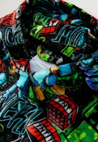 Fleece nightwear top featuring a black background with colorful graphics and patterns, including buildings and text elements. Label visible.