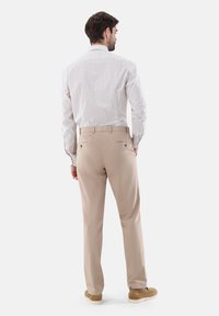 Beige Hose mit glatter Textur, seitlichen Taschen und taillierter Passform. Kombiniert mit einem hellen, karierten Hemd mit Knöpfen.