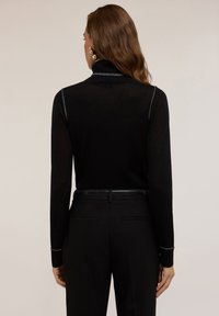 Pulover negru cu gât înalt și mâneci lungi, având accente metalice pe guler și cusături. Este purtat cu pantaloni negri la comandă.