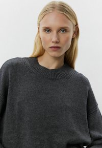 Maglione grigio scuro realizzato in un materiale morbido e testurizzato; presenta un collo a girocollo a costine e una vestibilità leggermente oversize. Nessun motivo o hardware visibili.