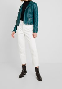 Turbkawona skórzana kurtka motocyklowa z zamek błyskawicznym z przodu, w połączeniu z białymi, krótkimi dżinsami i ciemnobrązowymi botkami za kostkę. Gładka tekstura i dopasowany krój.