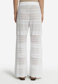 Białe koronkowe spodnie szerokie z nogawkami wyróżniają się skomplikowanymi, otwartymi wzorami i różnorodnymi fakturami, z wysokim stanem i luźnym krojem.