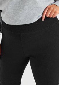 Mustat venyvät legginsit, joissa on ribbireunus, sileä pinta ja tiukka malli, yhdistettynä harmaaseen collegepaitaan vyötäröllä.