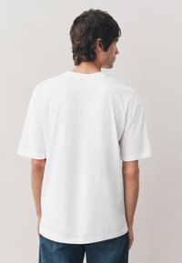 Vit bomulls-t-shirt med korta ärmar, rund halsringning, avslappnad passform, med en mjuk textur och enkel design. Bärs med blå denimjeans.