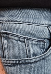 Light blue denim jeans close-up, featuring a back pocket with a distinct seam. Texture is slightly distressed with visible stitching details.