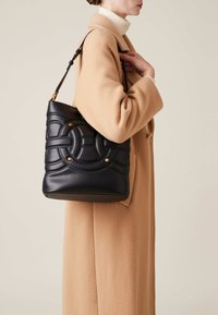 Black leather bucket bag with quilted design, gold hardware accents, and a textured surface, worn over a beige coat.