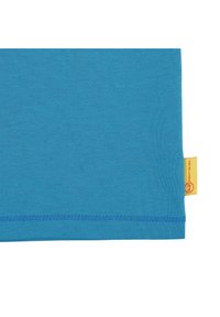 Textil de algodón turquesa con una textura suave, que presenta un dobladillo recto y una etiqueta amarilla con un logo rojo en el lateral.