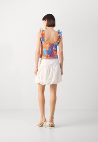 Haut floral multicolore avec des bretelles volantées, associé à une mini jupe blanche évasée. Le haut présente un design à dos carré.