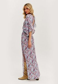 Prúžna, vzorovaná šaty v svetlom modrom s paisley vzorom. Obsahuje zapínanie na zaviazanie na chrbte a bočné rozparky. Model má na sebe hnedé čižmy po kolená.