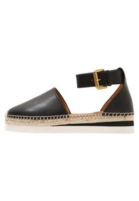 Espadrilles de cuero negro con tirante en el tobillo, plantilla de yute trenzado, punta redonda y suela de goma blanca. Presenta un detalle de hebilla dorada.