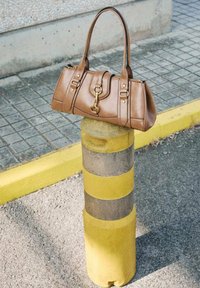 Brown leather handbag with a structured design, featuring dual handles, a front flap, gold hardware, and a smooth texture.