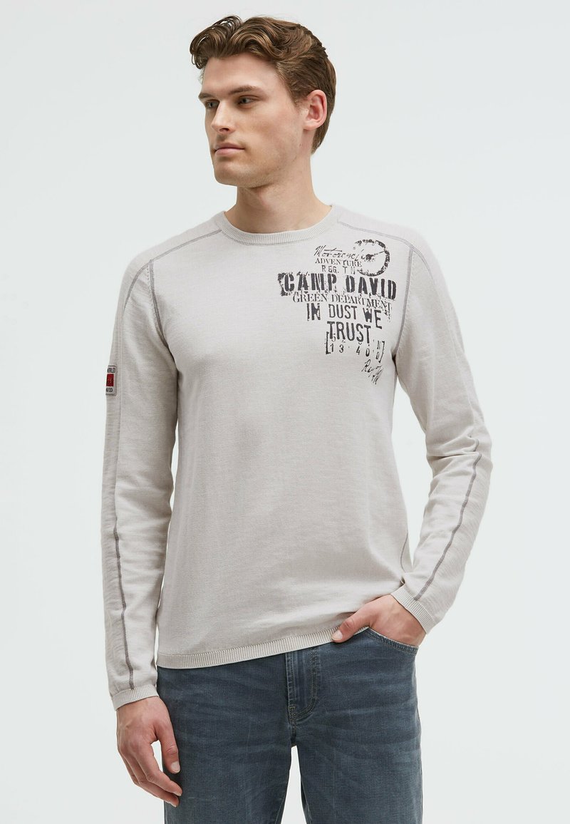 Helles graues Langarmshirt mit bedrucktem Text und grafischen Akzenten, strukturiertem Stoff, geripptem Kragen und kontrastierenden Nahtdetails.