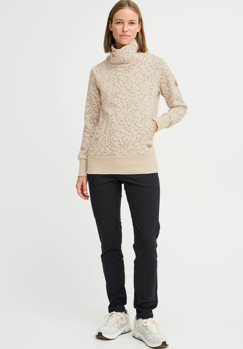 Felpa beige con collo alto e stampa floreale colorata. Polsini e orlo a costine. Abbinata a pantaloni neri e sneakers bianche.