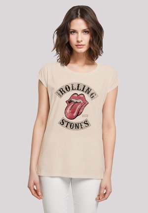 Light beige t-shirt with a round neck, short sleeves, featuring a bold red and black Rolling Stones logo graphic at the front.