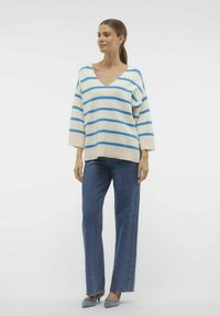 Gestreepte trui in crème met blauwe strepen, met v-hals en een losse pasvorm. Gecombineerd met recht-aflopende donkerdenim jeans en blauwe hoge hakken.