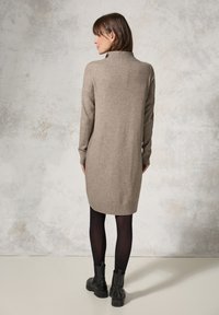 Abito in maglia beige con colletto alto, maniche lunghe, polsini e orlo a coste, abbinato a stivali neri alla caviglia.