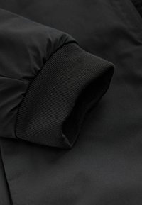 Mustan takin hiha, jossa on resorikäänne; sileä kangaspinta mattapintaisella viimeistelyllä. Sisältää puhtaan, minimalistisen muotoilun.