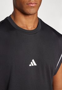 Black athletic sleeveless shirt with a round neckline, made of textured fabric, featuring a white Adidas logo on the chest.