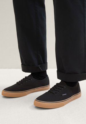 Schwarze Canvas-Sneaker mit einer strukturierten Gummisohle, runden Zehen, Schnürdesign und subtiler Markenkennzeichnung an der Seite.