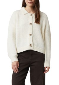 Biały dziergany kardigan z kołnierzem, sześcioma dużymi guzikami i ściągaczami przy rękawach. Luźny fason z krótszym dołem. Miękka faktura.