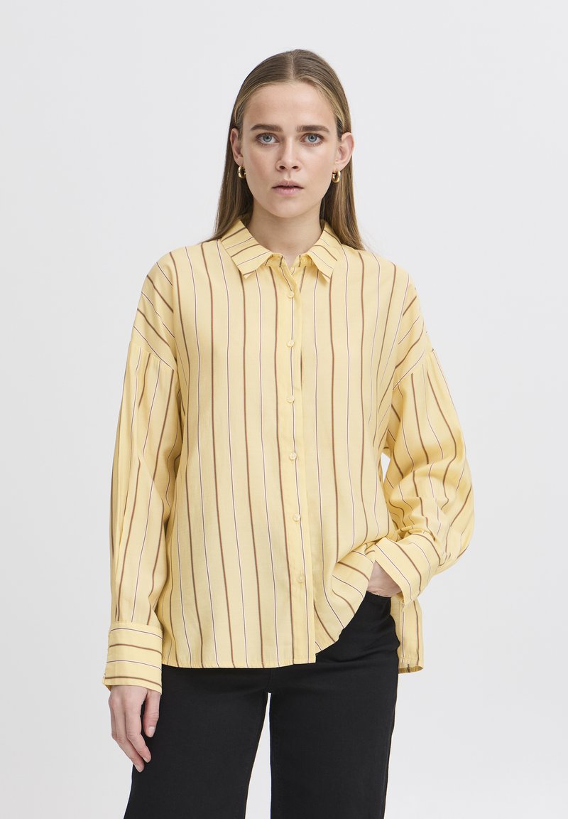 Camicia a righe gialle con chiusura a bottoni, colletto alla francese e maniche lunghe leggermente a sbuffo. Presenta righe verticali color bordeaux per un contrasto.