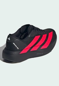 Scarpa sportiva nera con accenti a righe rosa, tomaia in rete testurizzata e una spessa suola in gomma nera. Presenta il logo del marchio sul tallone.