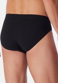 Slip di cotone nero con vestibilità aderente, dotato di una cintura liscia e cuciture pulite. Design semplice senza motivi visibili o elementi hardware.