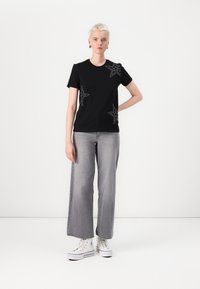 Black t-shirt with short sleeves, featuring silver star embellishments; paired with loose grey jeans and white sneakers.