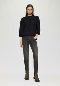 Schwarze, plissierte Bluse mit Puffärmeln, kombiniert mit dunkelgrauen, schmal geschnittenen Jeans und braunen Stiefeletten mit einer dicken Sohle.