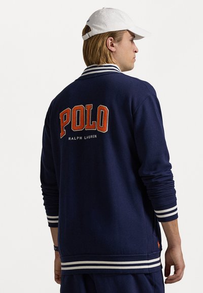 Navy blue sweatshirt with striped ribbed cuffs and hem, featuring "POLO" and "Ralph Lauren" embroidered in orange on the back.