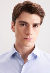 Camicia abbottonata in tessuto azzurro chiaro, con colletto classico, patta frontale e una texture sottile. Vestibilità liscia e su misura.