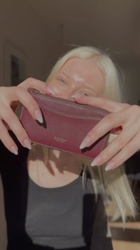 Burgundy leather wallet with a zip closure, featuring a smooth texture and subtle curves. Gold "COACH" branding on the front.