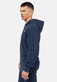 Marineblauer Kapuzenpullover aus weichem Material, mit gerippten Bündchen und Saum, Reißverschluss und kleinem Logo auf der Brust.