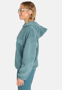 Turquoise fleece hoodie met een gestructureerd oppervlak, voorzien van een trekkoordkap en geborduurd logo. Zachte stof en ontspannen pasvorm ontwerp.