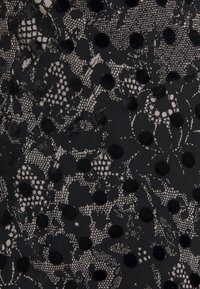 Czarna tkanina z kwiatowym wzorem z koronki i wypukłymi czarnymi kropkami. Tekstura jest skomplikowana, łącząc gładkie i dotykowe elementy.