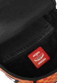 Interior negro con líneas de un bolso de patrón naranja y negro, con un bolsillo de malla y una etiqueta roja con texto. Cierre con cremallera.